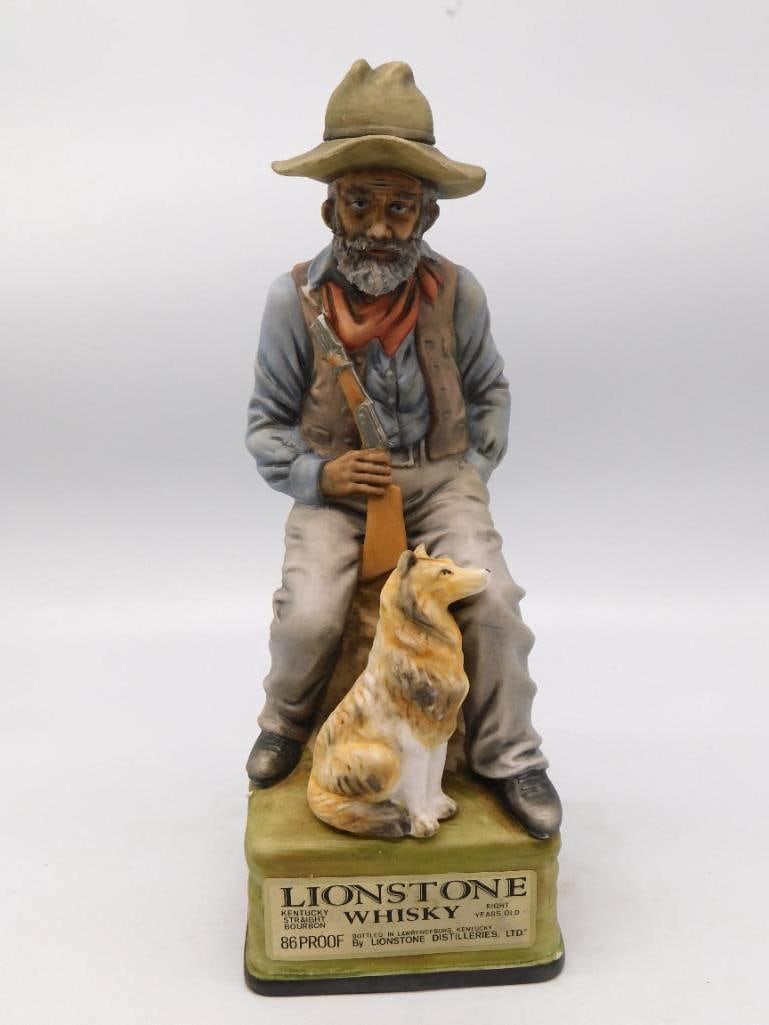 Lionstone Decanter, Seated Frontiersman: A Lionstone decanter modeled as a grey-bearded frontiersman seated on a green block with his rifle across his knee and a collie keeping watch at his side. The bisque body takes the paint well, and