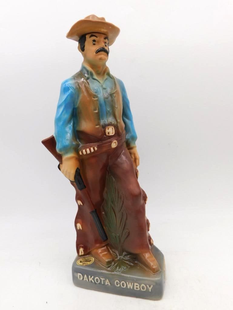 Heritage China Dakota Cowboy Western: A well-turned decanter modeled as a Dakota cowboy in leather chaps and blue work shirt, a rifle held at his side and his hat pulled low over a black mustache. The base is lettered Dakota Cowboy and