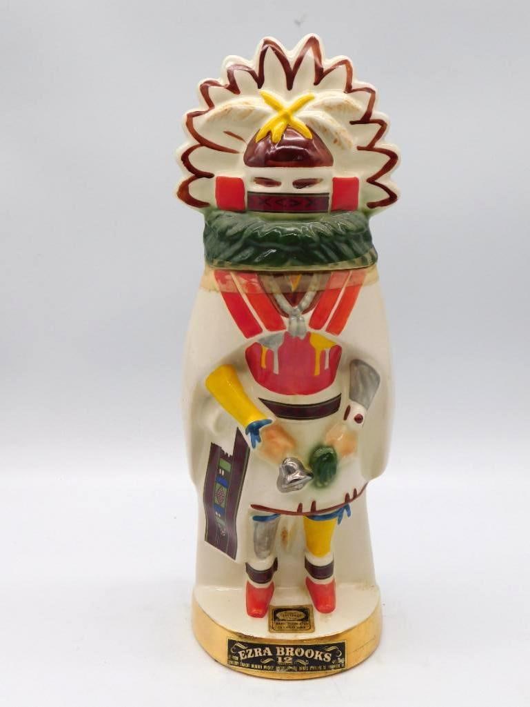 Ezra Brooks Kachina Dancer Decanter, 12: A ceramic decanter from Ezra Brooks sculpted as a Kachina Dancer, robed in white with red, yellow and blue detailing and red boots, a feathered sunburst cape spread behind him. A commanding piece that