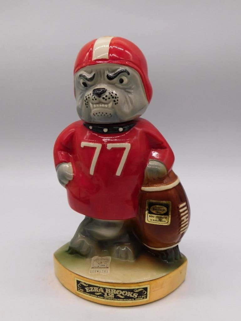 Ezra Brooks Football Player Number 77: An Ezra Brooks ceramic decanter modeled as a bulldog-faced football player in a red jersey numbered 77, the ball tucked under his arm and his jaw set for the line. Carries a hand-decorated 24-karat go