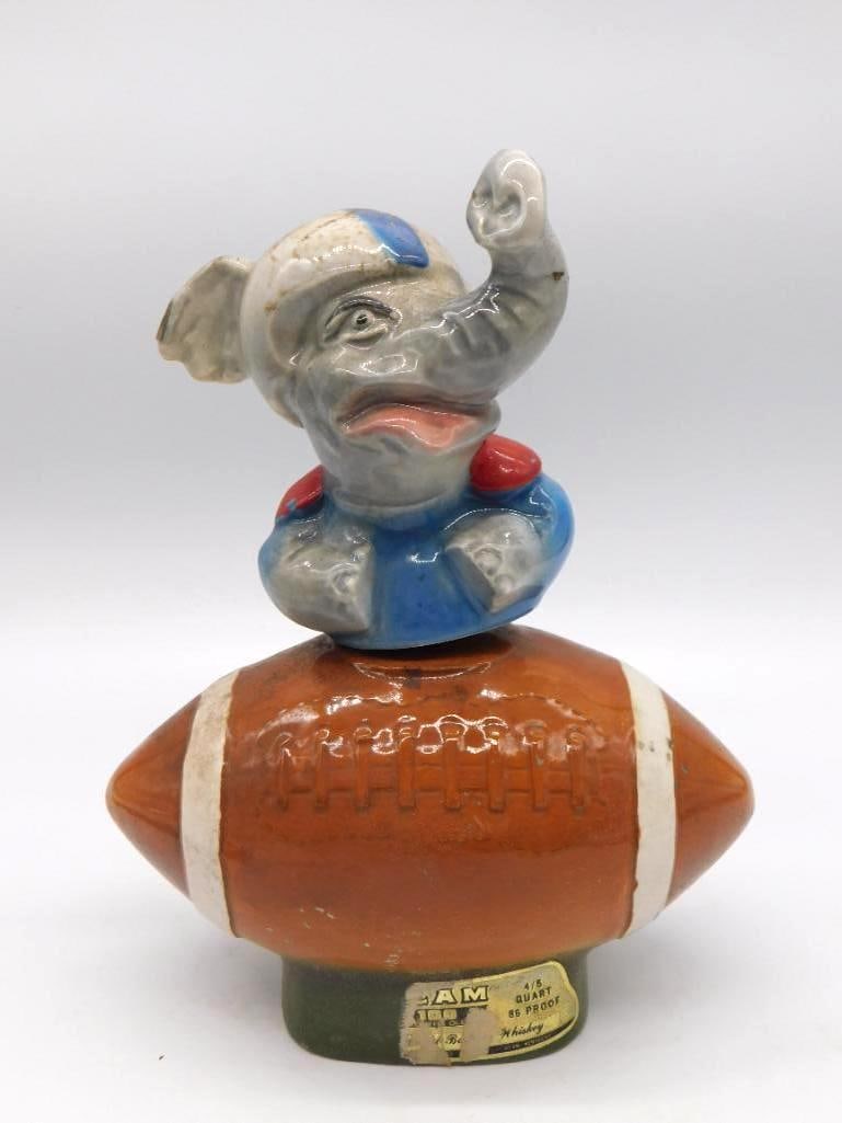Jim Beam Alabama Crimson Tide Elephant: A Jim Beam decanter modeled as the elephant mascot in a blue jersey, perched atop a football, a plain nod to the Alabama Crimson Tide. The Kentucky Straight Bourbon Whiskey label survives in part to t