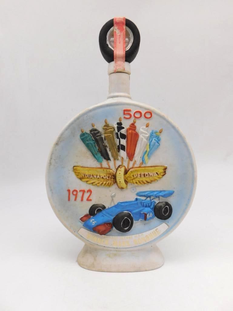 Jim Beam Indianapolis 500 1972 Mark: A Jim Beam ceramic decanter commemorating the 1972 Indianapolis 500, its face raised with a blue race car among checkered and racing flags and set with an applied gold-tone portrait medallion. The rev