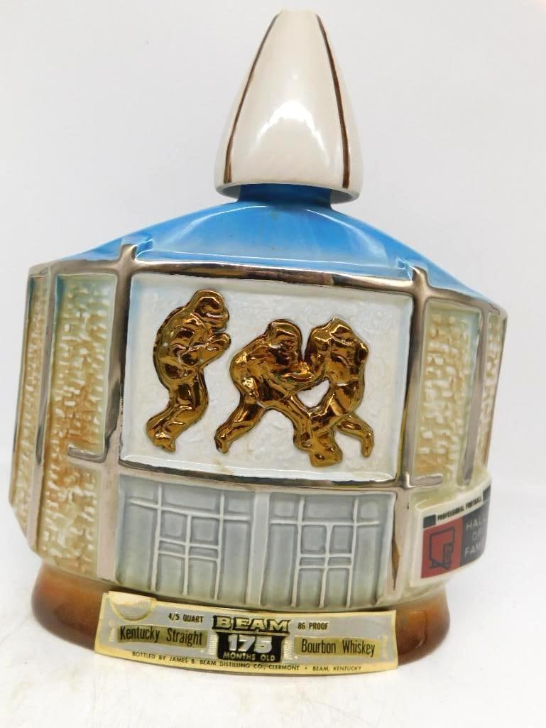 Jim Beam Professional Football Hall of: A Jim Beam decanter honoring the Professional Football Hall of Fame, the front panel bearing three gilt gridiron players in relief within the building's facade and the small Hall of Fame emblem at