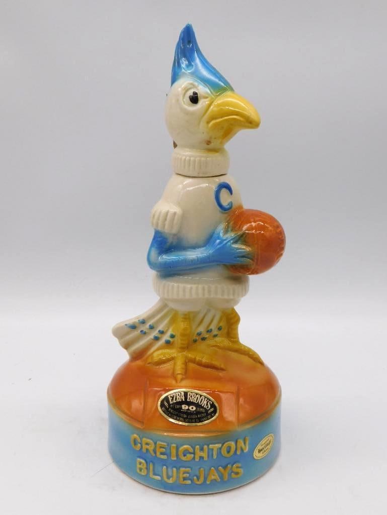 Ezra Brooks Creighton Bluejays: A stout Ezra Brooks decanter modeled as the Creighton Bluejays mascot in a white and maroon team sweater, a basketball held close. A lively bit of collegiate sculpture with genuine presence on a