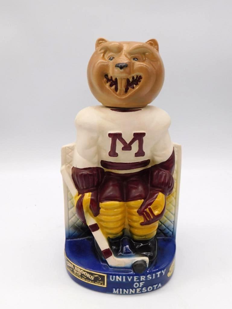 Ezra Brooks University of Minnesota: An Ezra Brooks decanter sculpted as the Minnesota Golden Gophers hockey mascot in maroon and gold, hockey stick and puck in hand. A lively piece with genuine presence on a shelf. The base is marked