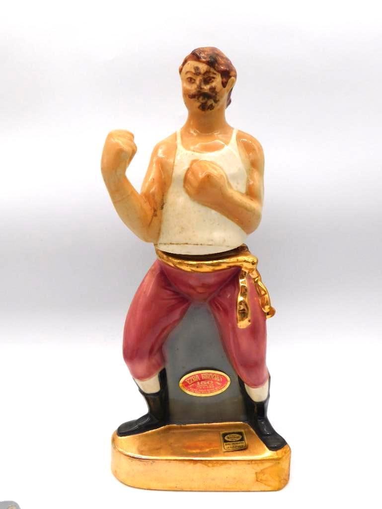 Ezra Brooks Bare-Knuckle Boxer Decanter: A stout Ezra Brooks ceramic decanter modeled as a bare-knuckle boxer squared up in fighting stance, fists raised and jaw set. The sculptor caught a genuine spirit of the ring, and the painter did not