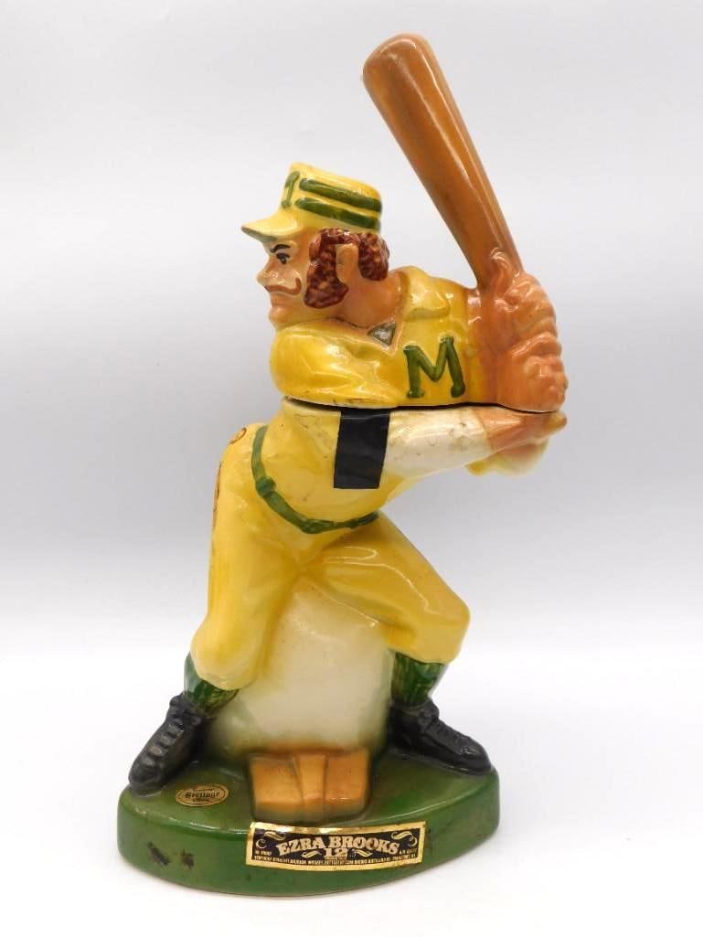 Ezra Brooks Baseball Batter Ceramic: A spirited Ezra Brooks decanter modeled as a baseball batter in vintage flannels, an "M" worked onto the jersey front. The sculptor caught him mid-stance upon a green oval base, and the paint has