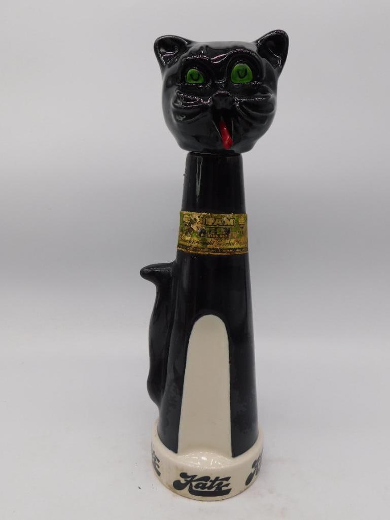 Black Glass Cat Decanter, Green Eyes and: A black glass decanter modeled as a seated cat with a long upright tail forming the handle, painted green glass eyes, a red bow, and a gold-tone collar. No maker's mark is visible in the photos