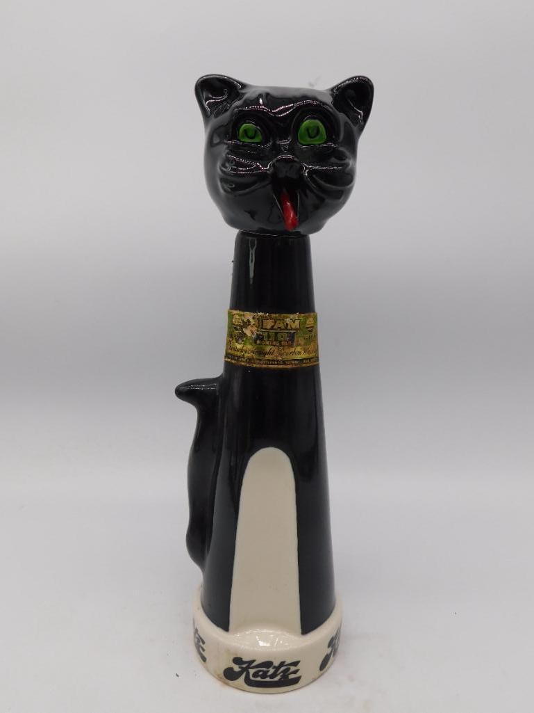 Black Glass Cat Decanter, Green Eyes and: A black glass decanter modeled as a seated cat with a long upright tail forming the handle, painted green glass eyes, a red bow, and a gold-tone collar. No maker's mark is visible in the photos provid