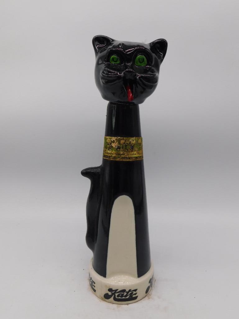 Black Glass Cat Decanter, Green Eyes and: A black glass decanter modeled as a seated cat with a long upright tail forming the handle, painted green glass eyes, a red bow, and a gold-tone collar. No maker's mark is visible in the photos