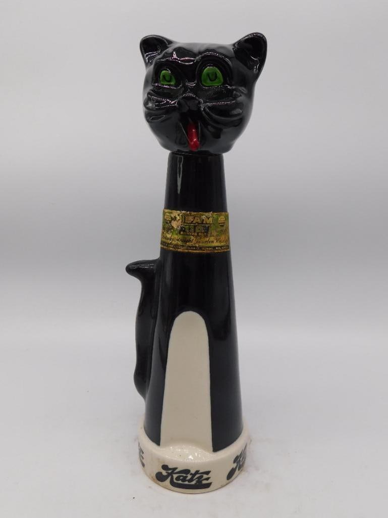 Black Glass Cat Decanter, Green Eyes and: A black glass decanter modeled as a seated cat with a long upright tail forming the handle, painted green glass eyes, a red bow, and a gold-tone collar. No maker's mark is visible in the photos