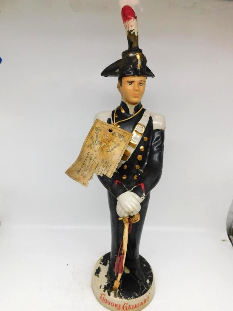 Liquore Galliano Italian Carabiniere: A commanding Liquore Galliano decanter modeled as an Italian carabiniere at attention in full dress, bicorne hat and plume above, gloved hands resting upon the hilt of his sword. The original printed