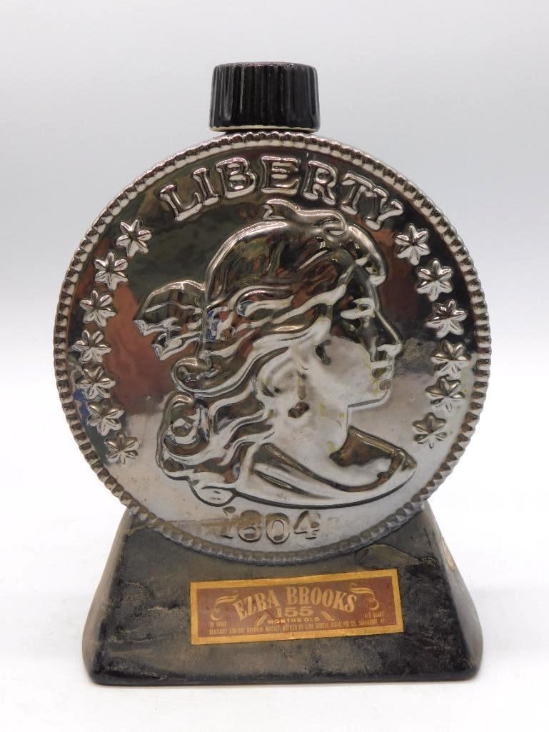 Ezra Brooks 1804 Liberty Coin: A second example of the Ezra Brooks ceramic decanter cast as an 1804 Liberty coin, finished in silver-tone upon a black base. A clever conceit, and the relief holds its crispness admirably. The gold