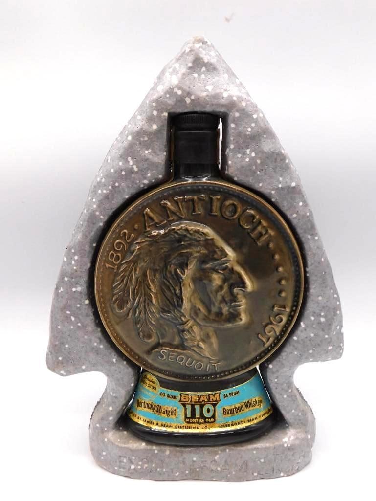 Jim Beam Antioch Illinois 1967 Diamond: A Jim Beam ceramic decanter in the form of an arrowhead, struck for the 1967 Diamond Jubilee marking the seventy-fifth year of Antioch, Illinois. A relief coin medallion carries a Native American prof