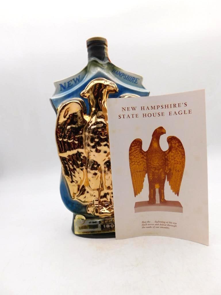 Jim Beam New Hampshire State House Eagle: A Jim Beam Regal China decanter in blue, mounted with a raised gold eagle honoring the State House Eagle of New Hampshire. An informational card describing the statue accompanies it, and the original 