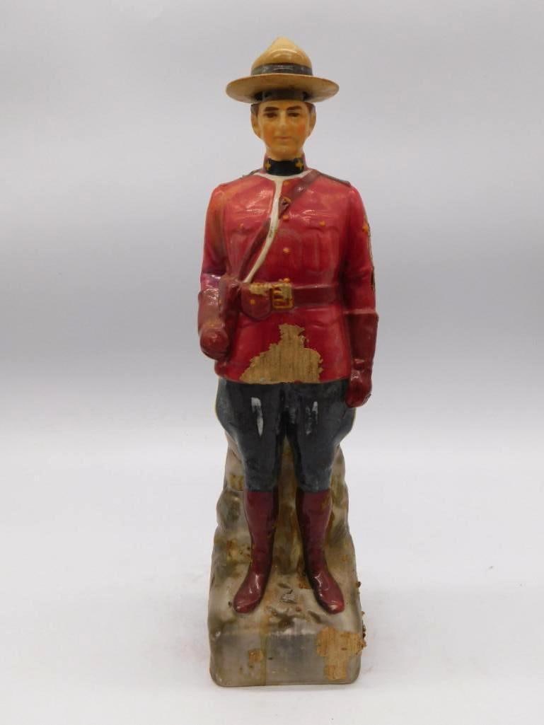 Royal Canadian Mounted Police Mountie: A ceramic decanter sculpted as a Canadian Mountie in red serge dress uniform and campaign hat, standing upon a rock-textured base. Approximately 12 inches tall. Noticeable paint loss to the red coat