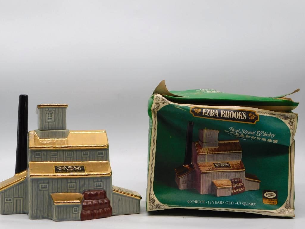 Ezra Brooks Distillery Building Decanter: An Ezra Brooks decanter molded as the distillery itself, a stepped warehouse in gray clapboard with a tall black stack, gilt roofs, and a rick of barrels at the loading door. The gold has kept its