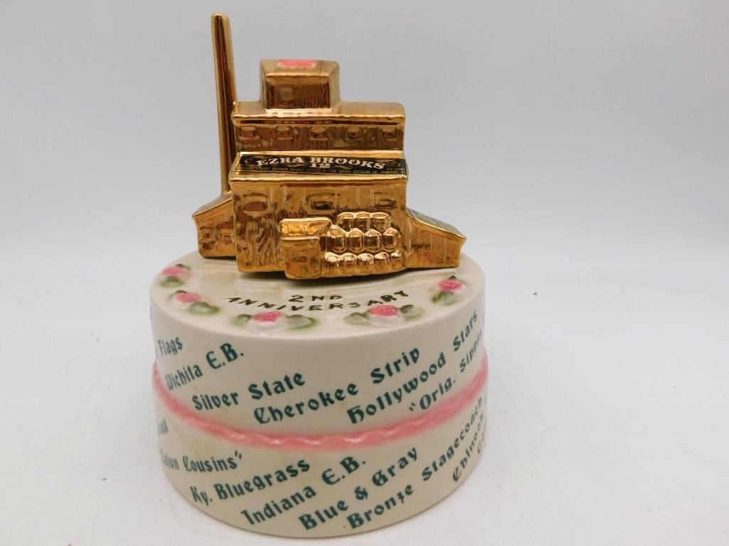 Ezra Brooks 2nd Anniv. Bottle Club: An Ezra Brooks decanter struck for a collectors second anniversary, the gold distillery building perched atop a modeled cake ringed with roses and lettered over with club and bottle names, among them 