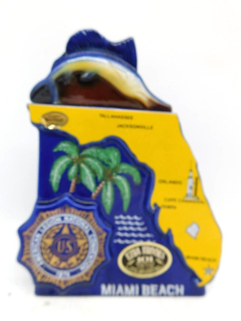 American Legion 56th Natl Convention: A commemorative decanter cut in the outline of the State of Florida, glazed cobalt and gold with palms, the American Legion emblem, and the principal cities named across the map. A sailfish serves as 