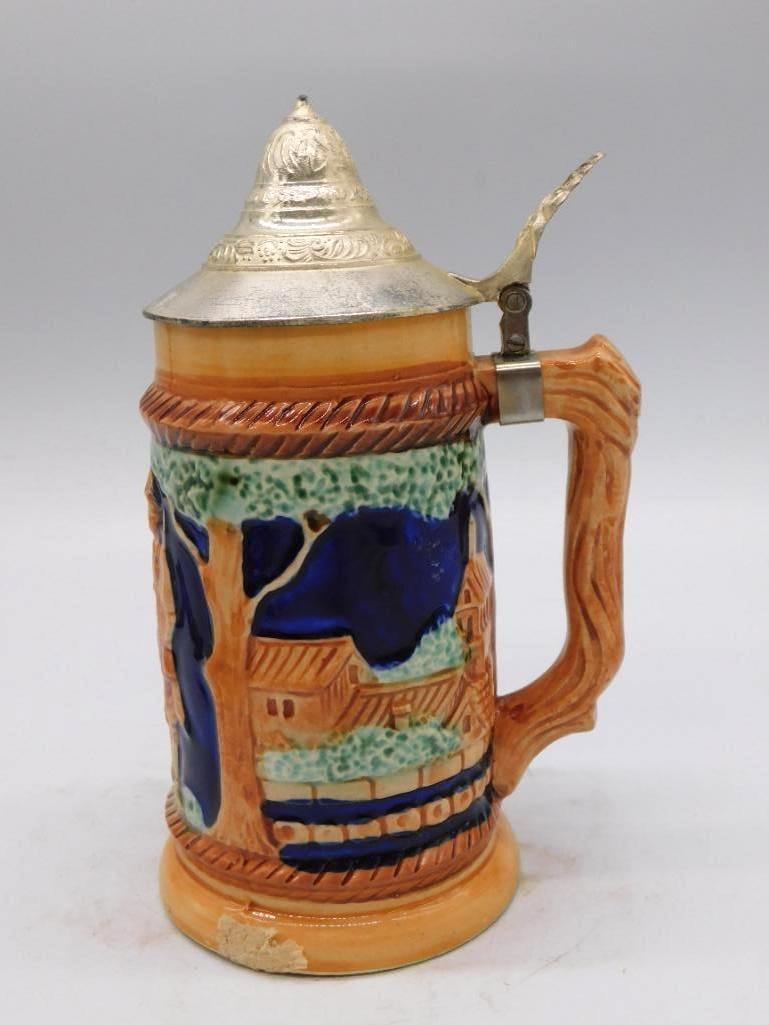 German-Style Ceramic Stein Decanter with: A ceramic novelty decanter shaped as a German stein, one of a small matching group in this collection. The cobalt blue relief carries a village scene, and the piece is fitted with a wood-grain handle