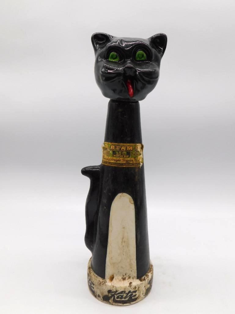Jim Beam Black Cat Katz Ceramic Decanter: A Jim Beam ceramic decanter in the form of a stylized black cat, green glass eyes set in his head and a red tongue showing, with a gold 'Beam' neck label. A jaunty piece standing approximately 13