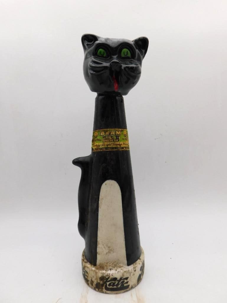Jim Beam Katz Black Cat Ceramic Decanter: A Jim Beam Regal China decanter in the form of a stylized black cat, green-eyed with a red tongue, marked Katz to the base and retaining the original gold Beam bourbon label at the neck. A sleek and
