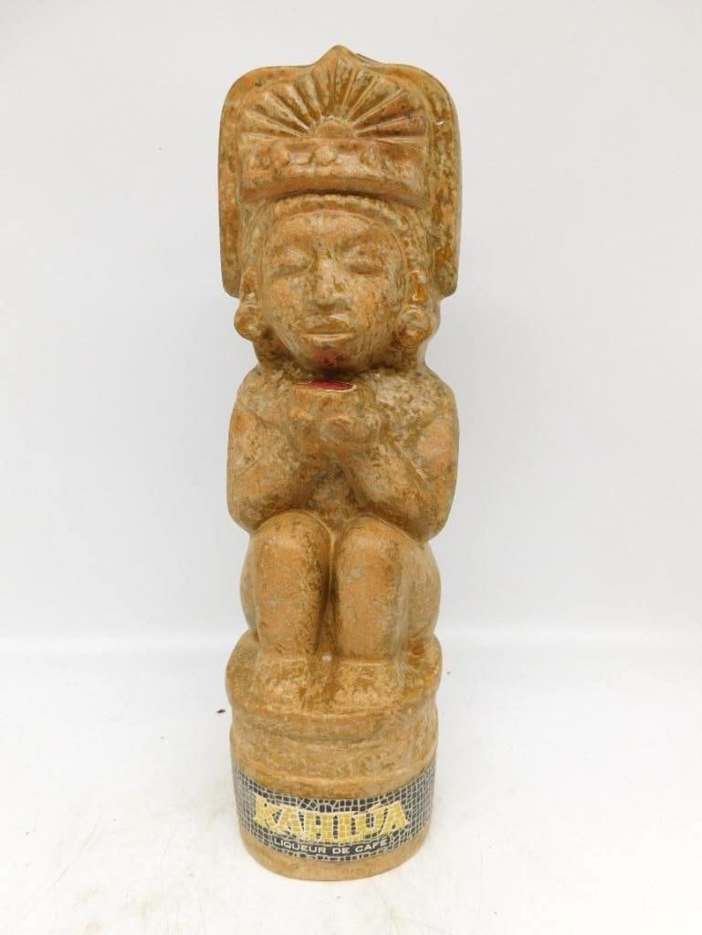Kahlua Liqueur Bottle Modeled as a: A Kahlua Liqueur de Cafe bottle cast as a seated deity in a broad plumed headdress and ear spools, hands drawn to the chest, the whole finished in a mottled buff that imitates weathered stone. The mol