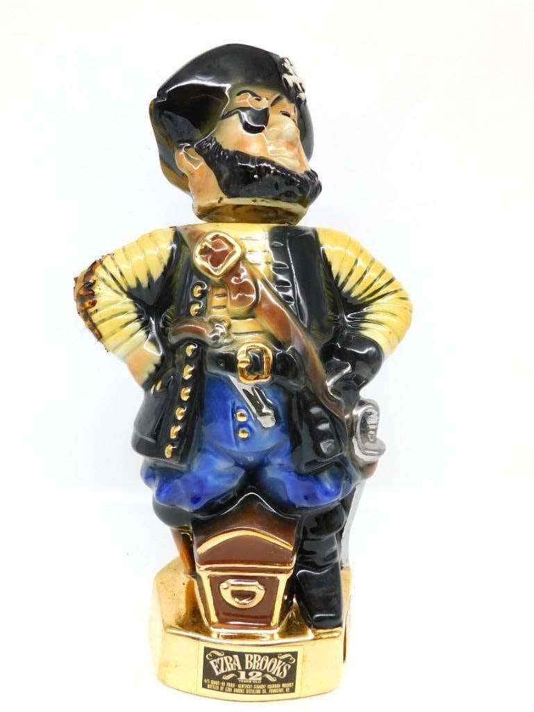Ezra Brooks Buccaneer Pirate Decanter: A jaunty Ezra Brooks decanter modeled as a bearded buccaneer in tricorn hat and eye patch, cutlass slung at his hip and a treasure chest at his feet, the whole standing on a gilt plinth.
