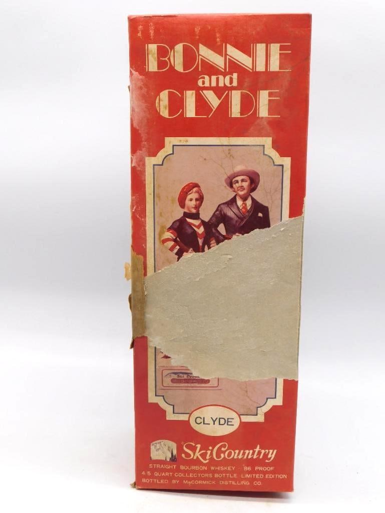 McCormick Ski Country Bonnie and Clyde: A McCormick Ski Country limited edition decanter from the "Bonnie and Clyde" series, this example a hand-painted skier in a blue and red outfit holding a rifle, marked "Clyde" on the original box.