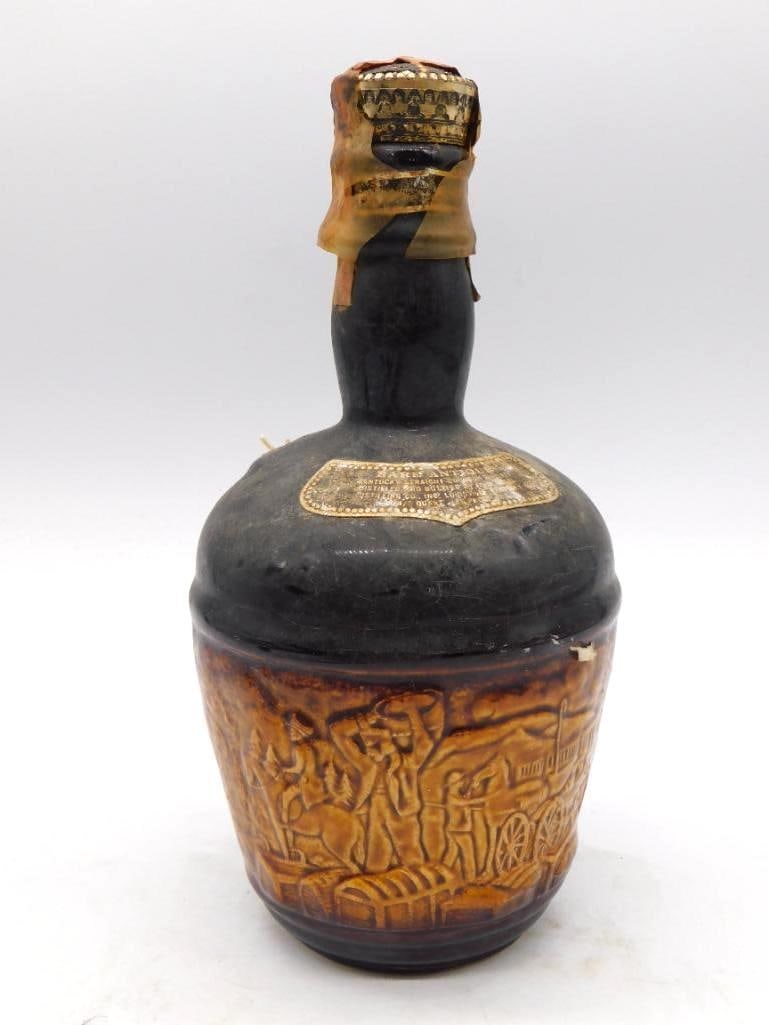 Conquistador Relief Stoneware Whiskey: A dark-glazed stoneware decanter, its body molded in relief with conquistadors, wagons and figures in procession, the shoulder and neck finished in black glaze. Measures approximately 9 inches long