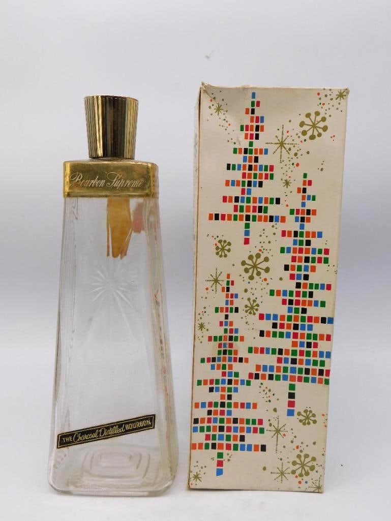 Bourbon Supreme Charcoal Distilled Cut: A trim tapered decanter in clear pressed glass, a cut starburst at the front and a gold-tone collar and fluted cap above. The collar is lettered Bourbon Supreme, with the black and gold Charcoal Disti