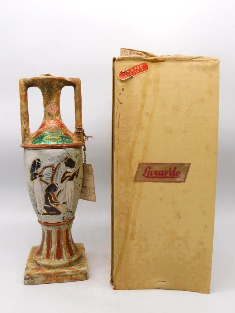 Luxardo Egyptian Amphora Cherry Wine: A stately Luxardo decanter in the form of an ancient amphora, twin handles rising above a body worked in relief with Egyptian musicians in gold and dark enamel. The mottled ochre glaze gives it the lo