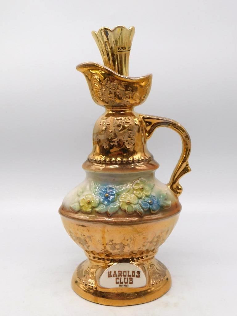 Harolds Club Reno Gold Luster Ewer: A well-turned ewer in gold luster, its shoulder set with applied blossoms in blue and yellow and its body worked over in gilt scroll. The scrolled handle and footed base are handsomely cast, and the p