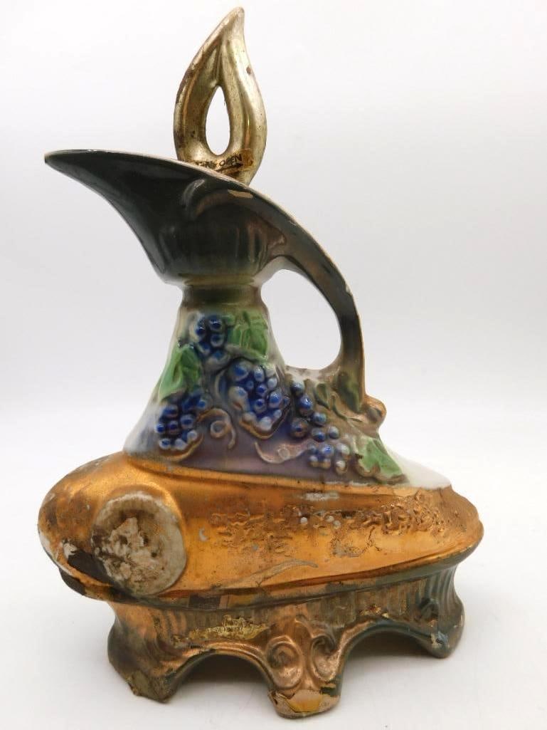 Gilt and Grapevine Ceramic Ewer Decanter: A large ewer-form decanter of ambitious design, the shoulder heavy with molded grape clusters and vine in blue and green, the swelling body and scrolled foot laid over in gold, and a pierced flame-sha