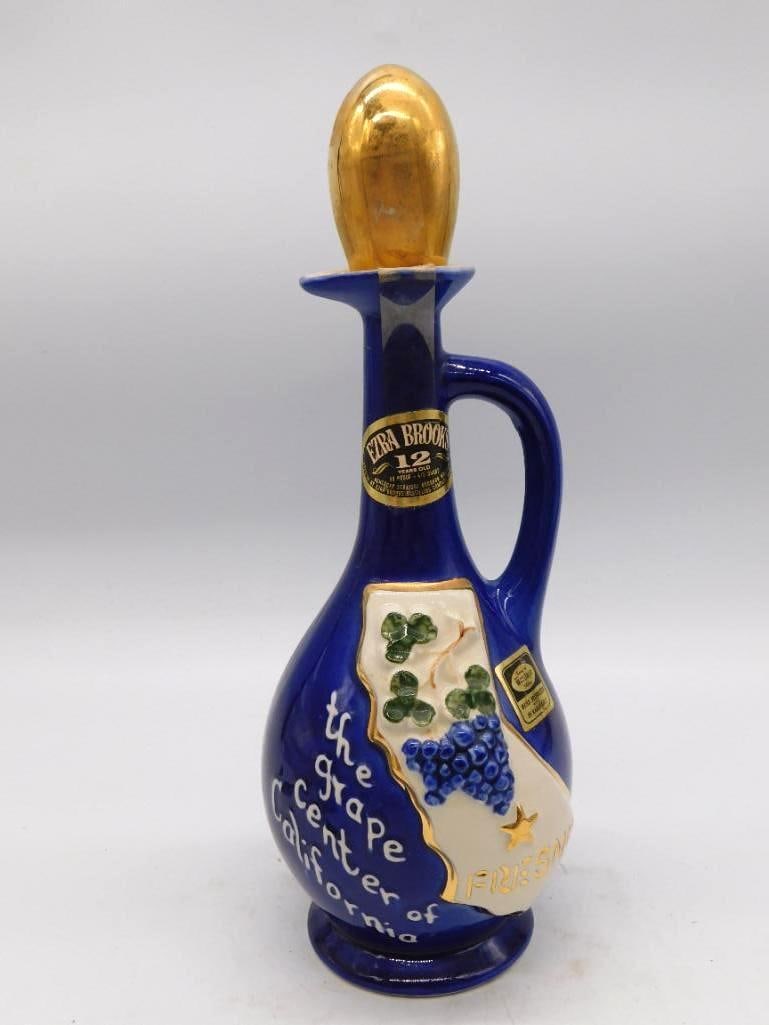 Ezra Brooks Cobalt Blue Grape Cluster: A handled Ezra Brooks decanter in deep cobalt, its body embossed with a cluster of grapes and lettered The Grape Center of California in flowing script. The gold-tone finial stopper is present.