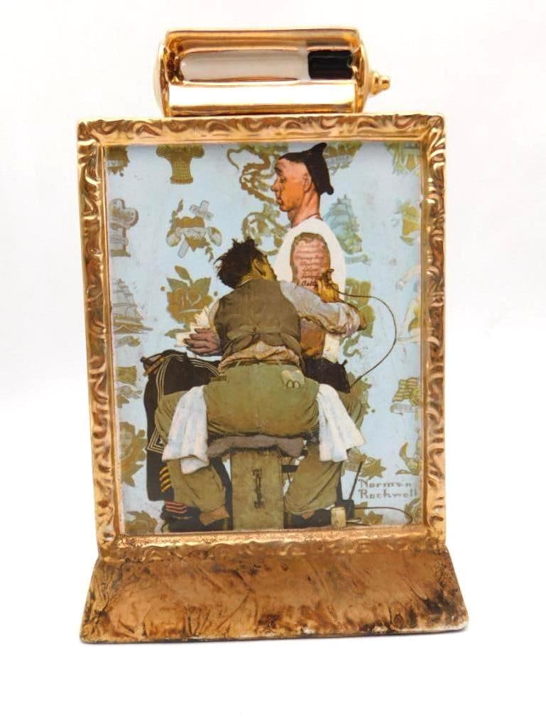 Norman Rockwell The Tattooist Ltd Ed: A limited edition ceramic decanter reproducing Norman Rockwell's "The Tattooist" from The Saturday Evening Post of 1944, set in a gold-tone frame with 23K gold trim. Bottled by The Mike Wayne