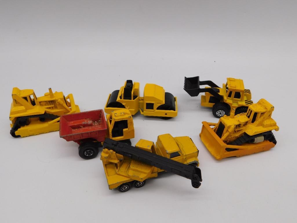Die-Cast Construction Toy Vehicle Lot: Group of seven yellow die-cast construction toy vehicles including a bulldozer, road roller, front loader, crane truck, and dump trailer, plus a red dump cart. Shows typical play wear, chipped paint,