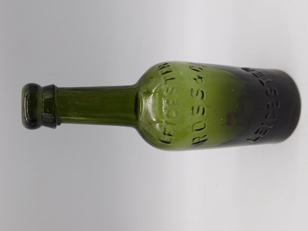 Antique Green Glass Bottle, Ross & Co Leicester: Dark olive-green glass bottle with applied lip closure, embossed 'Ross & Co, Leicester' along the body. Shows typical age wear, staining, and small surface imperfections from period manufacture.