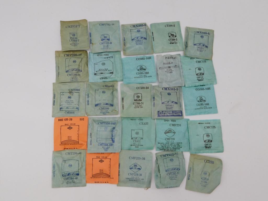 Antique Watch Crystals: 25 Assorted Vintage Glass Packets: Lot of 25 new-old-stock watch crystal packets in original manufacturer envelopes, branded for Bulova, Hamilton, Elgin, Longines, Witnauer and other makers, each printed with part number and millimeter