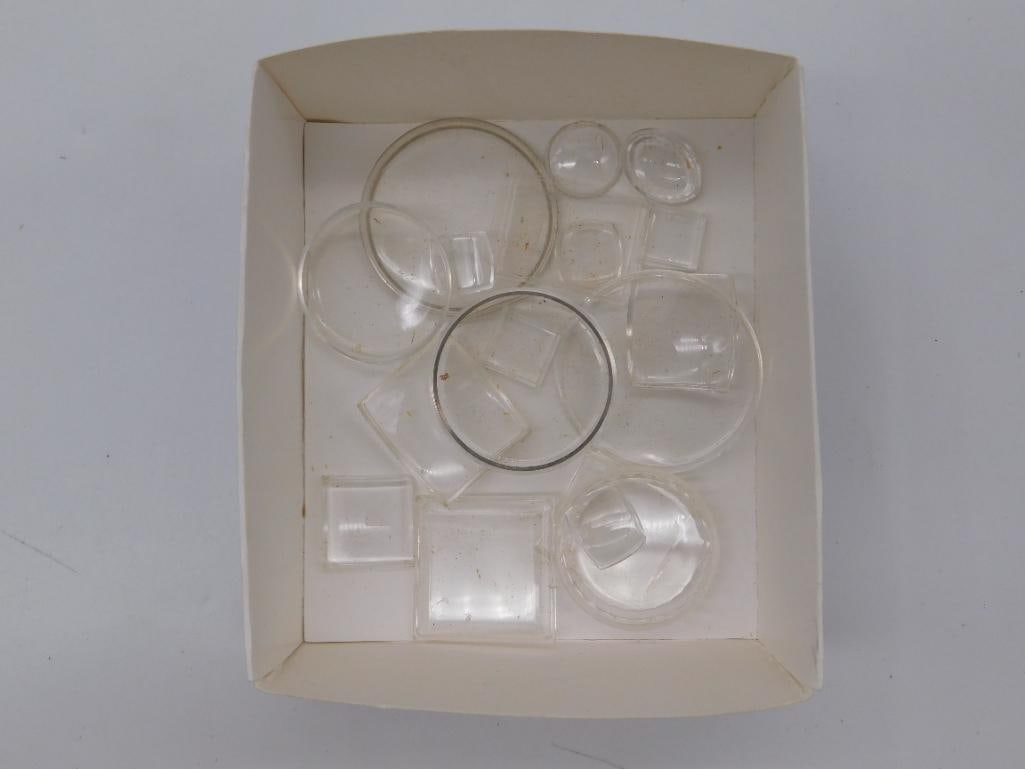 Antique Watch Crystals: Second Box Lot of Vintage Glass: A second cardboard box of assorted loose vintage watch crystals in round and square shapes, including one crystal with a metal tension ring, ranging from approximately 0.5 to 1.5 inches (quarter shown