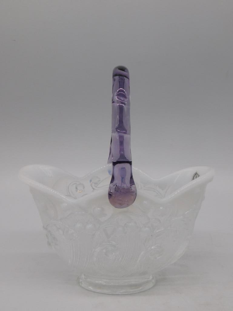Fenton Milk Glass Basket with Amethyst Handle, 100th Anniversary: White milk glass basket with a scalloped, crimped rim and an embossed floral lattice pattern, fitted with a twisted amethyst loop handle, by Fenton Art Glass. The base carries the oval Fenton mark and