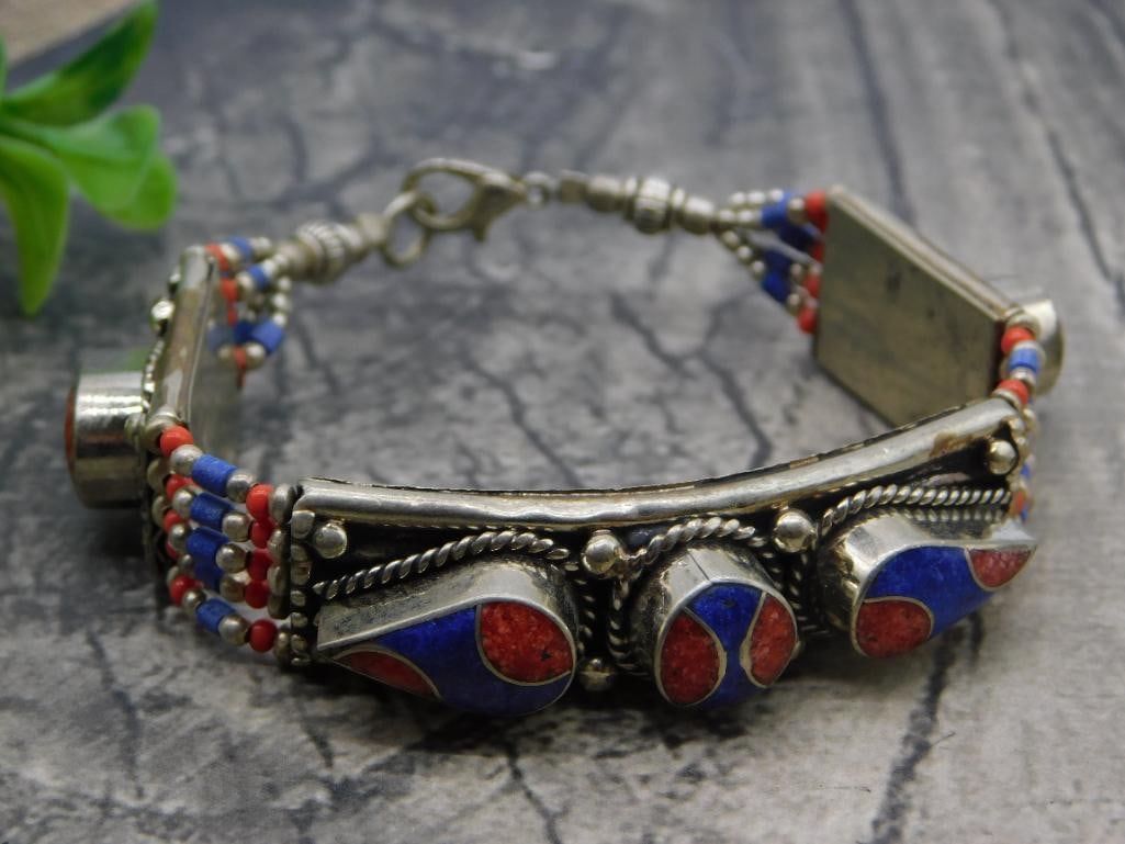 Bracelet Tibetan Silver Lapis Coral Inlay: Ethnic tribal-style cuff bracelet in white metal with inlaid lapis lazuli and coral-colored teardrop cabochons, accented by beaded side panels and a hook clasp. Measures approximately 7 inches long