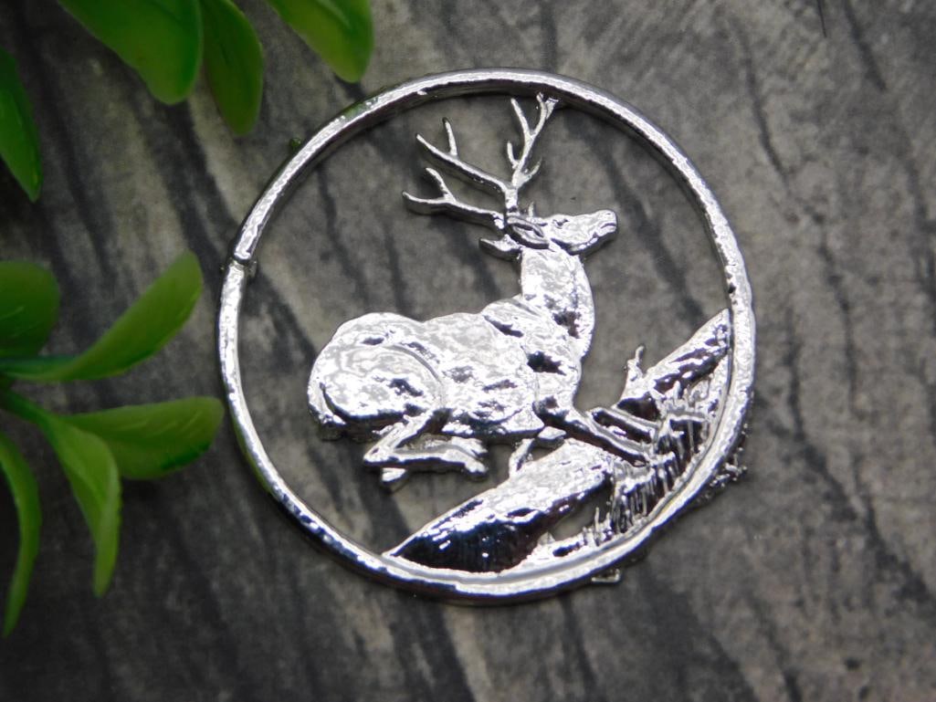 Medal - Silver-Tone Stag Deer Cut-Out Medallion Pendant: Round silver-tone medallion pendant with an open cut-out design depicting a resting stag with antlers beside a rocky outcrop. Measures approximately 1.5 inches in diameter, shown beside a quarter for 