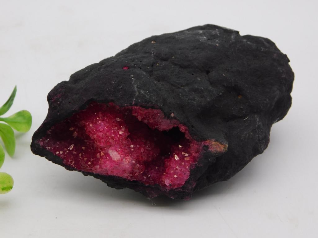 Crystal Geode - Pink Druzy Quartz Specimen, 198 Grams: Natural geode specimen with a dark exterior shell opening to reveal a cavity lined with sparkling pink druzy crystal formations. Weighs 198 grams and measures roughly 4 x 2.5 inches, shown with a quar
