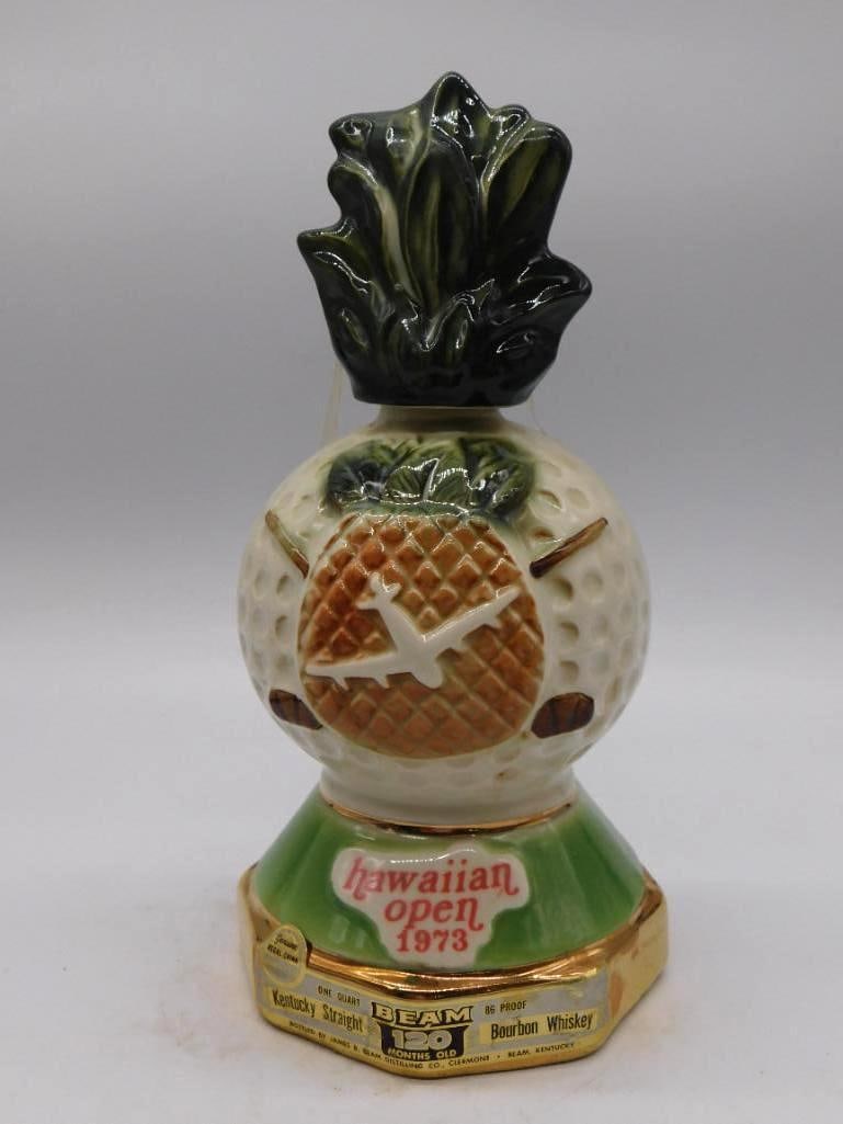 Jim Beam 1973 Hawaiian Open Golf Ball: A Jim Beam ceramic decanter shaped as a golf ball resting upon its tee, struck for the 1973 Hawaiian Open golf tournament sponsored by United Air Lines. A green pineapple-leaf stopper crowns it.