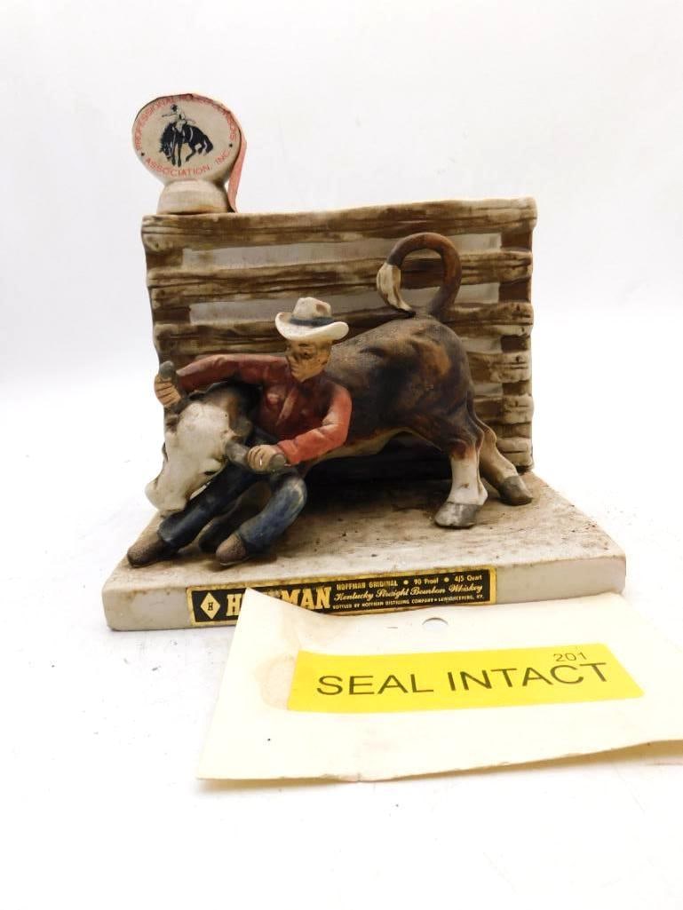 Hoffman PRCA Rodeo Steer Wrestling: A Hoffman Original decanter modeled as a rodeo hand throwing a steer before a corral fence, the cowboy's jaw set and the animal's weight well caught. The reverse panel lists the steer wrestling champi