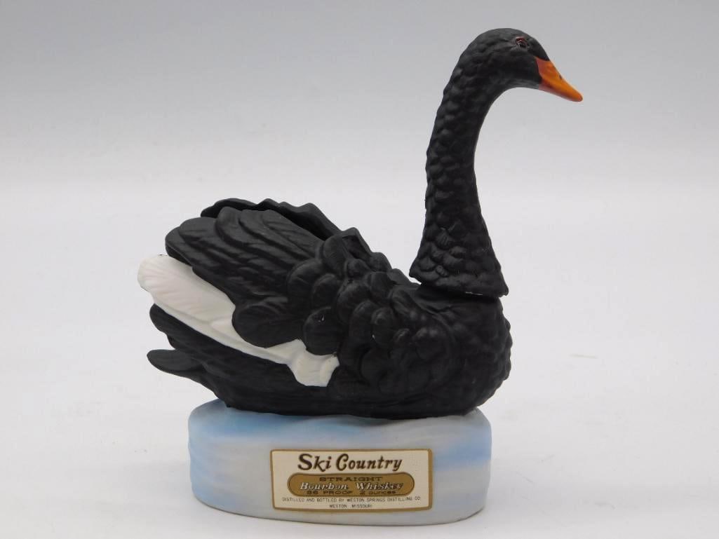 Ski Country Black Swan Decanter: A Ski Country straight bourbon whiskey decanter modeled as a black swan, orange bill lifted, riding a light blue water-effect base. Small, trim, and shrewdly observed by the sculptor. Ceramic,