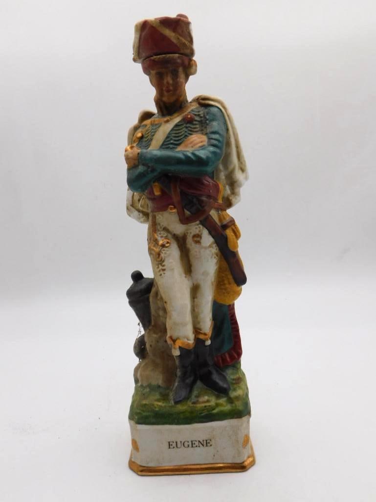 Grenadier Eugene Napoleonic Soldier Porcelain Decanter Dated 1969: A handsome Grenadier porcelain decanter modeled as the officer Eugene arms folded across a braided teal tunic fur cap set square and a cannon at his heel. The painter worked with a shrewd eye and the 
