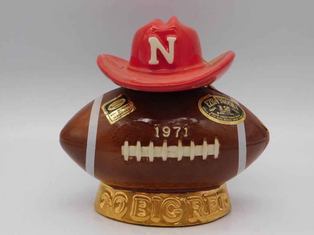 Ezra Brooks Nebraska Cornhuskers Go Big Red 1971 Football Decanter: An Ezra Brooks decanter shaped as a football and crowned with a Nebraska Cornhuskers red hat the gold-decorated lettering declaring 1971 and Go Big Red. A spirited keepsake of a Cornhusker season and