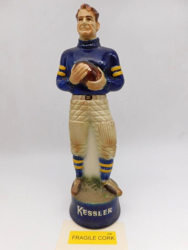 Kessler Football Player Ceramic Whiskey Decanter Fragile Cork: A Kessler ceramic decanter modeled as a football player of the old leather-pad era the ball tucked under his arm and a blue jersey with gold stripes upon his back. A stout subject plainly done and the